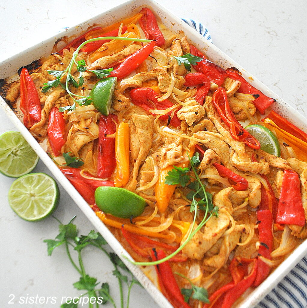 A large baking sheet with baked chicken fajitas, with peppers and limes. 