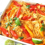 A sheet pan filled with strips of chicken, colorful peppers, and sliced limes.