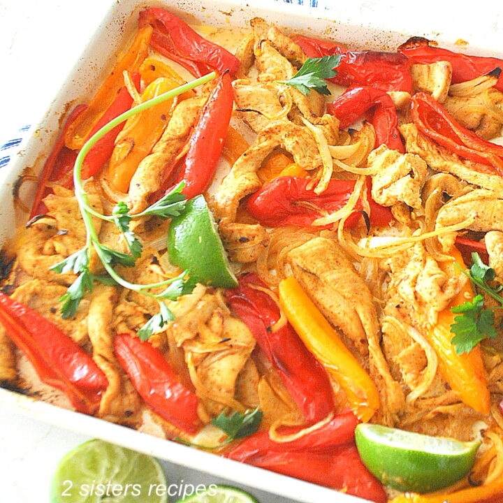 A large sheet pan with baked chicken strip and colorful peppers.