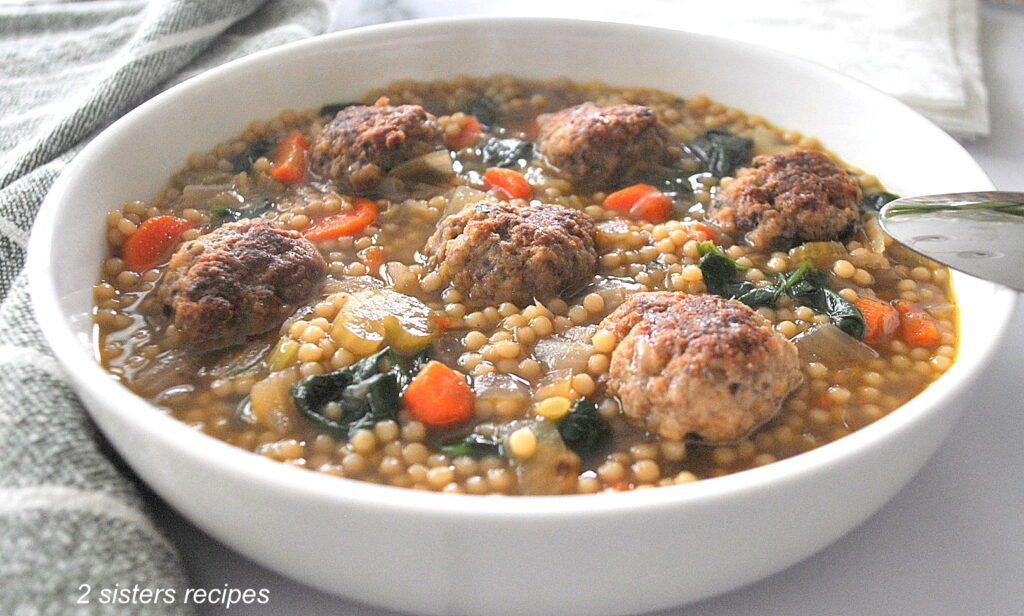 A white bowl of meatballs, Italian pastina, and veggie filled soup.