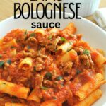 A white plate filled with rigatoni pasta topped with lamb bolognese sauce.