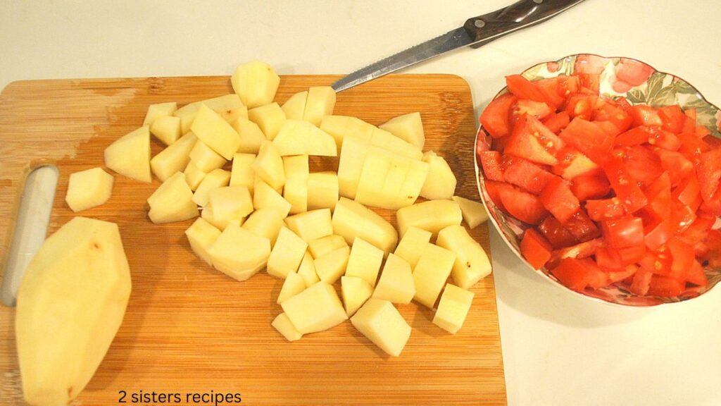 Potato and tomato is chopped on a wooden cutting board.