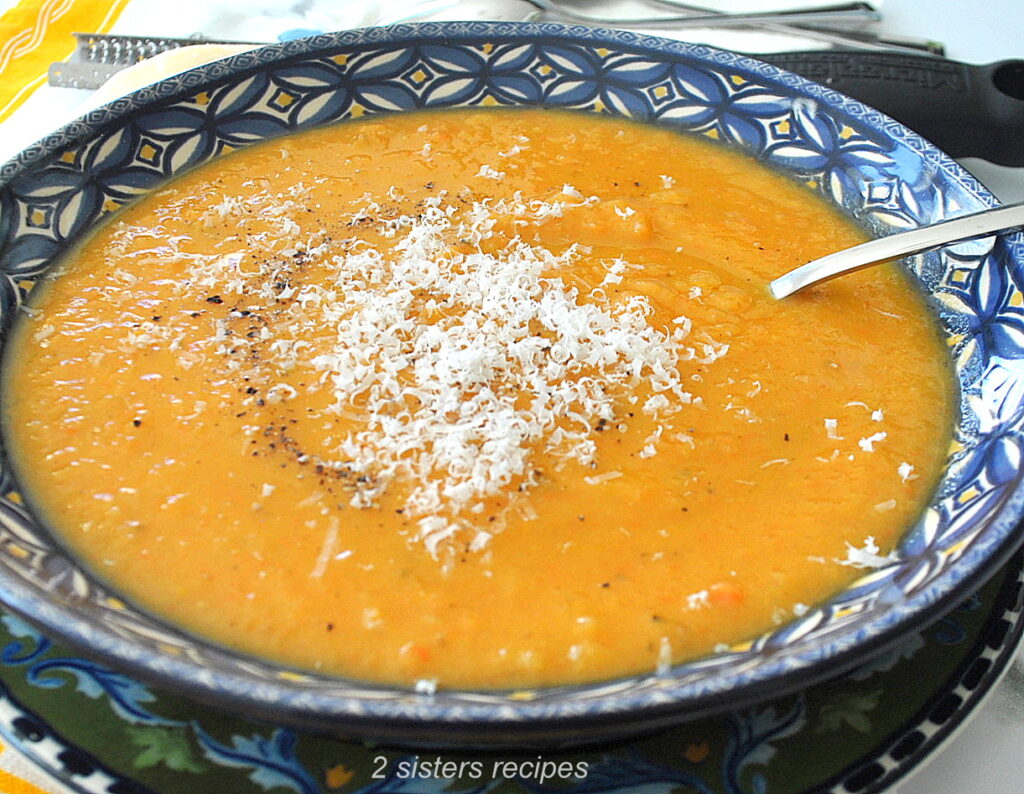 A blue bowl filled with pureed sweet potato soup with grated cheese on top. 