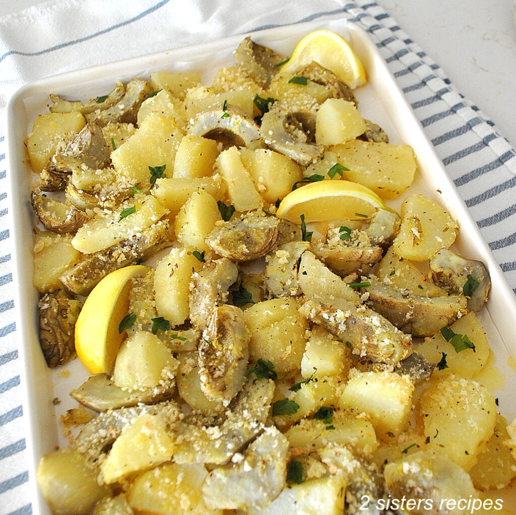 A large sheet pan with roasted potatoes and artichoke bottoms with lemon wedges.