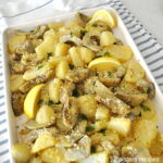 A large sheet pan with roasted potatoes and artichoke bottoms with lemon wedges.