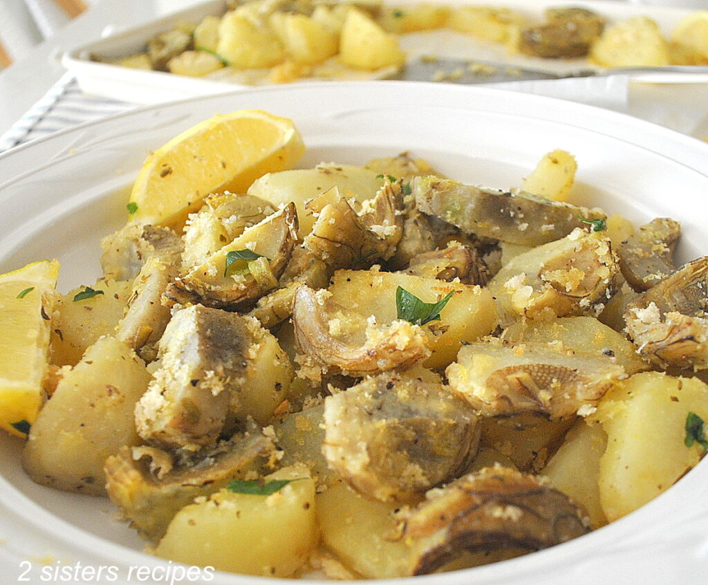 A round white platter filled with roasted sliced artichoke bottoms and potatoes.
