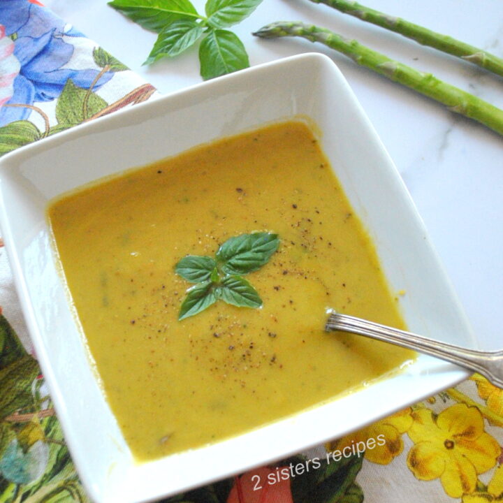 A white square bowl filled with pureed asparagus and basil soup with a spoon.