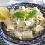 A blue plate filled with a short rigatoni pasta mixed with a creamy white sauce.