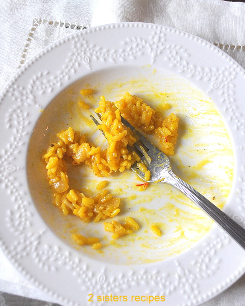 A white pasta bowl with a fork and some remaining yellow risotto in the dish.