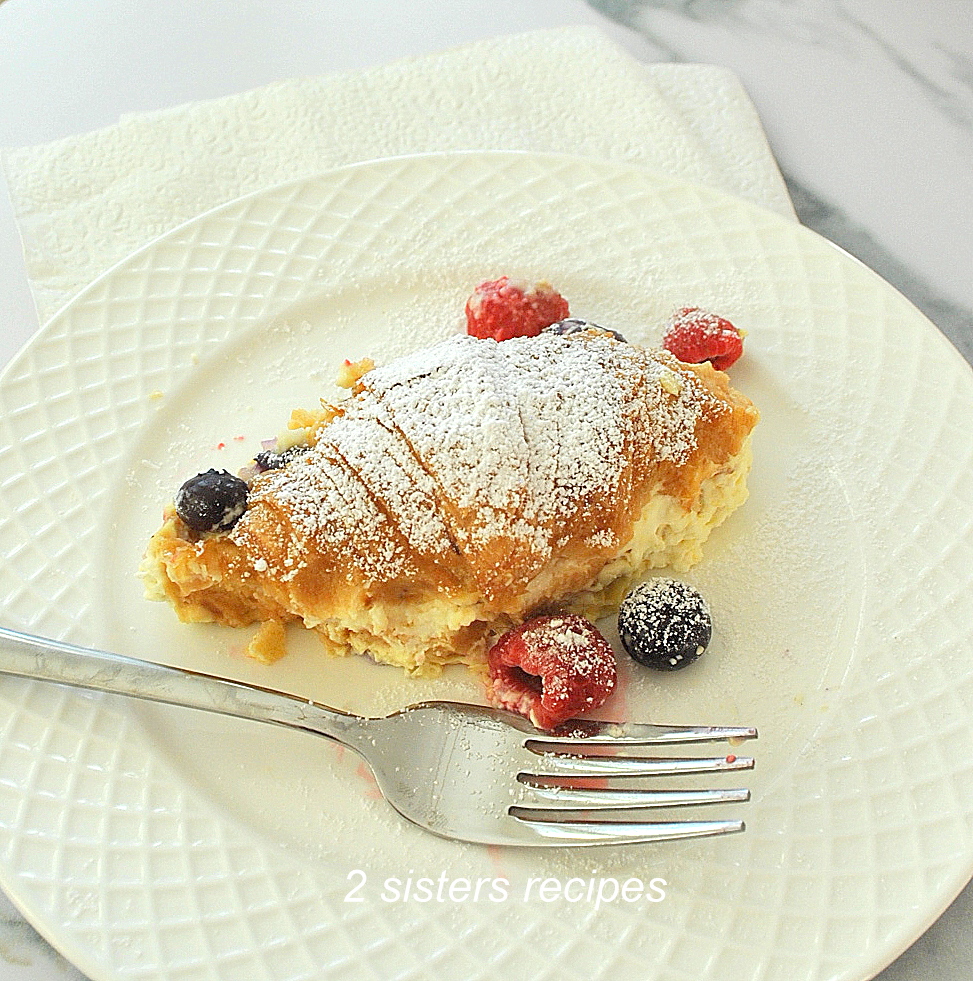 A white plate with a serving of a croissant filled with custard cream and berries.