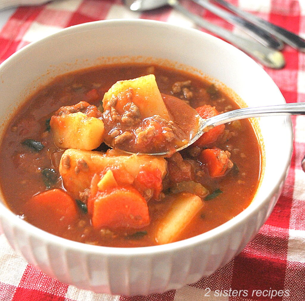 A white bowl filled with ground beef, chunks of potatoes, carrots and tomato broth,.