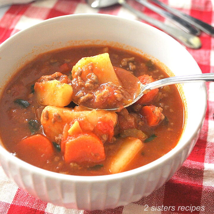 A white bowl filled with ground beef, chunks of potatoes, carrots and tomato broth,.