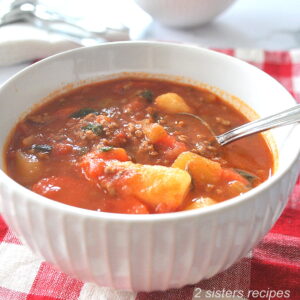 A white bowl filled with veggies, ground beef in a tomato broth.