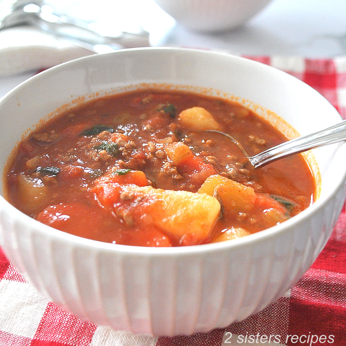 A white bowl filled with veggies, ground beef in a tomato broth.