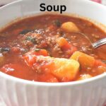 A white bowl filled with hearty hamburger soup and a spoon inside the bowl.