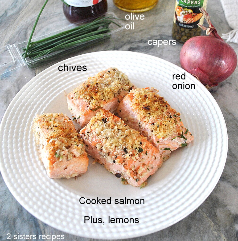 A white plate with 4 pieces of cooked salmon, and red onion and capers.