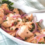 A oval serving dish filled with a cooked salmon salad with capers.