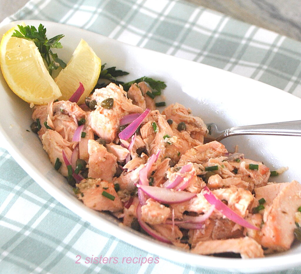 A white oval serving bowl filled with a salmon salad with lemon wedges/