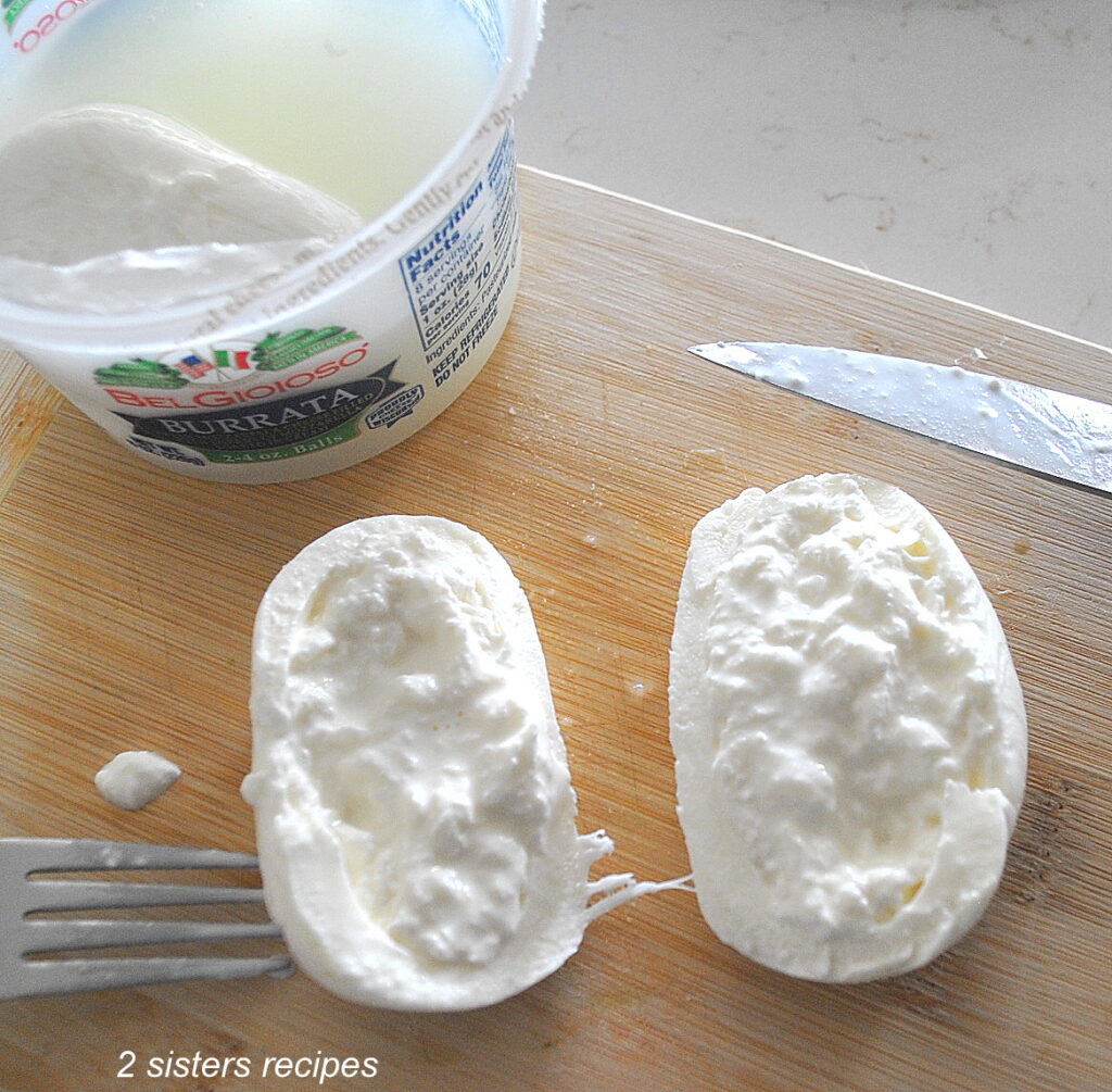 A burrata cheese ball sliced in half on a wood cutting board.