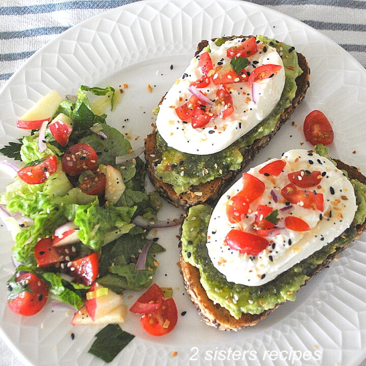 Two avocado and burrata cheese toasts on a white plate with a side salad.