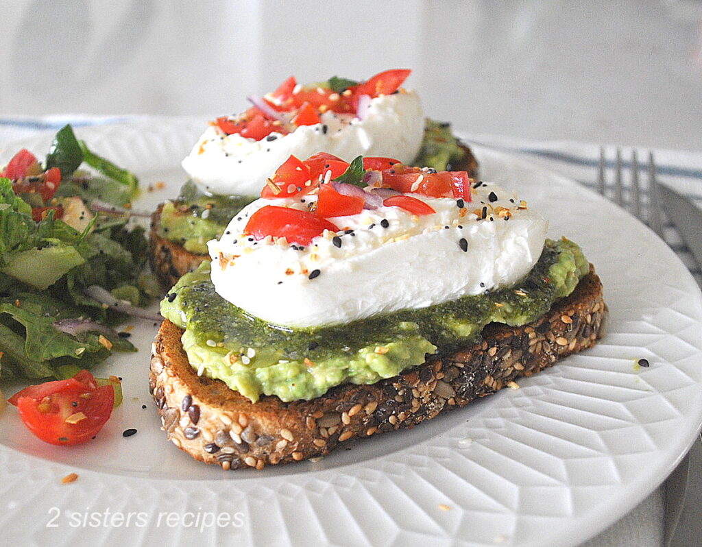 Two cheese and avocado toasts served on a white plate.