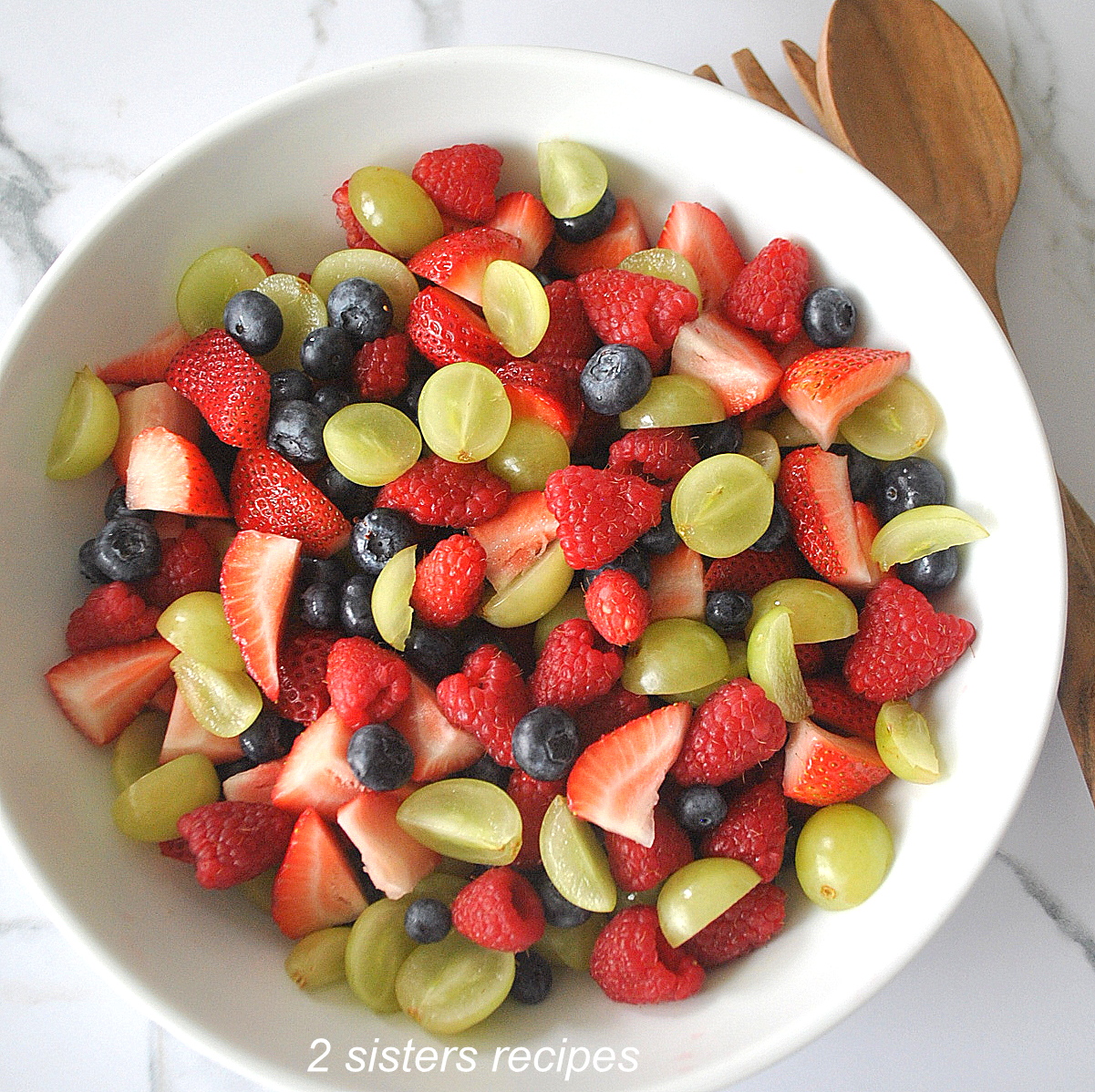 A white bowl filled with fresh berries, and sliced grapes.