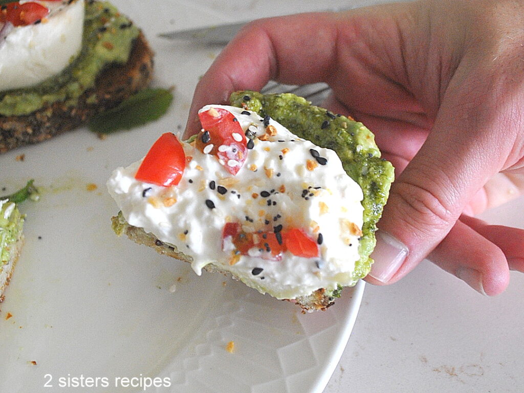 Someone is holding a burrata and avocado toast. 