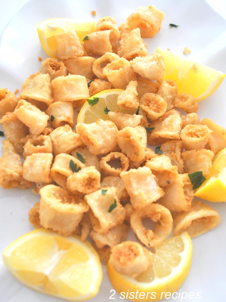 A white platter filled with fried calamari with lemon wedges on the side.