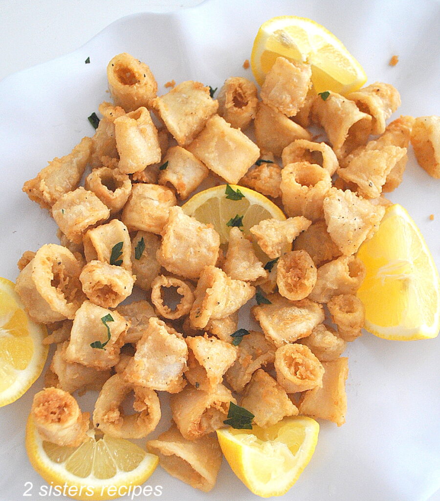 A white serving platter filled with fried calamari with lemon wedges on the side.