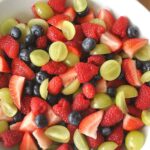 A white bowl filled with a mixture of fresh berries and grapes.