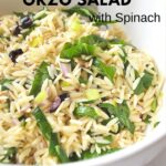 A large white bowl filled with orzo salad with ribbons of spinach and olives.