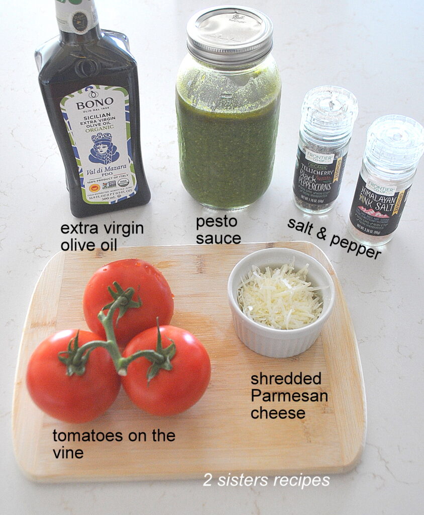 A cutting board with 3 tomatoes on the vine, and bottle of EVOO, a jar of pesto sauce, and salt & pepper.