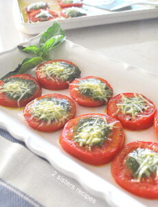 A white long platter with slices of tomatoes topped with some pesto sauce and cheese.