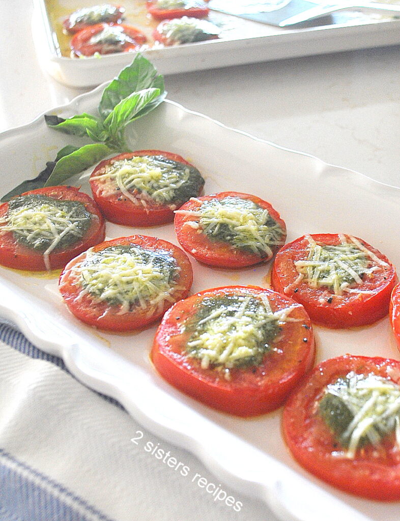 A white long platter with slices of tomatoes topped with some pesto sauce and cheese.