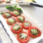 A white platter filled with baked sliced tomatoes topped with pesto and cheese.