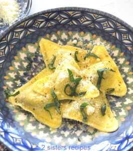 A blue dish with 5 ravioli with cheese and basil on top.