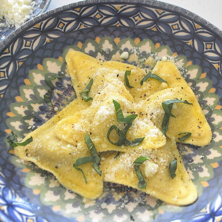 A blue dish with triangle shaped ravioli with grated cheese on top.