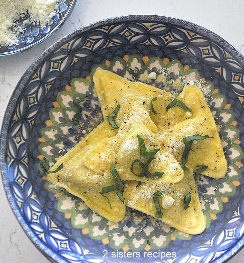 A blue dish with triangle shape ravioli with cheese and basil on top