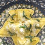 A blue plate filled with ravioli topped with cheese and fresh basil.