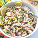 A white bowl filled with a white bean and tuna salad with lemon wedges on the side.