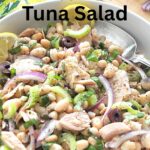 A white bowl filled with a white bean tuna salad with a spoon.