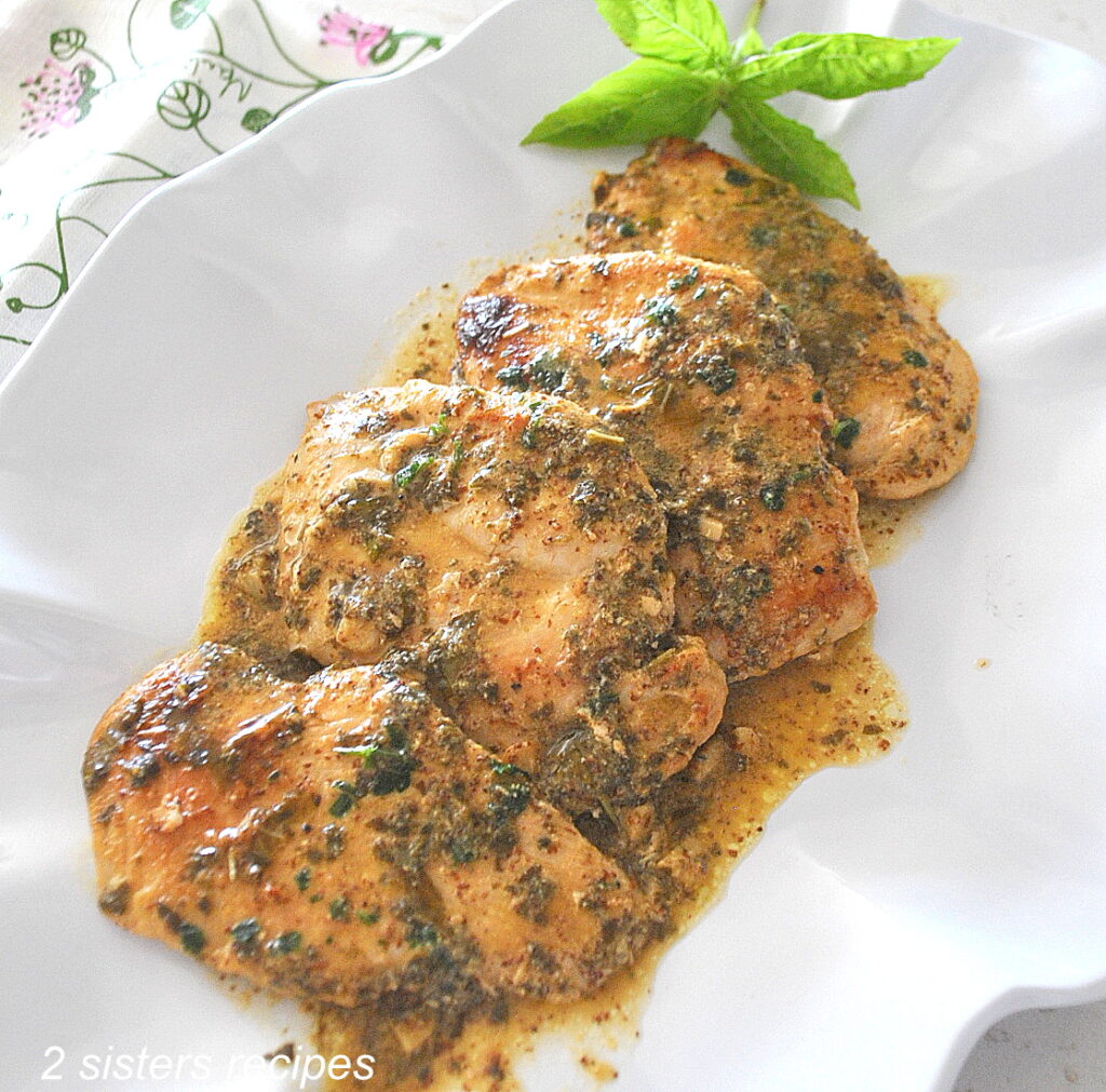 Four chicken cutlets cooked and covered with a mustard herb sauce served on a white platter.