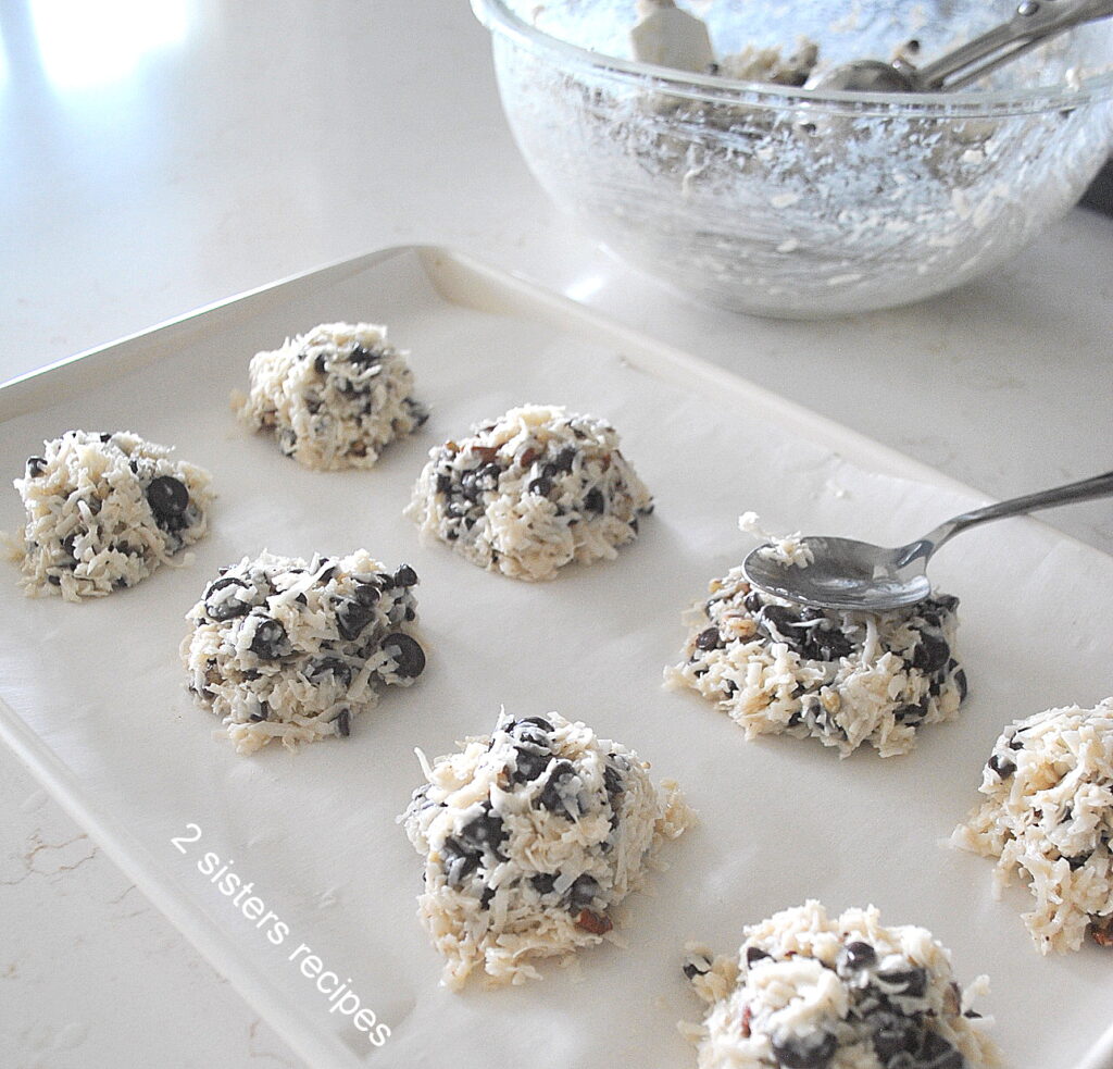 A cookie sheet with cookie batter and a spoon to tell them flattened tops down.