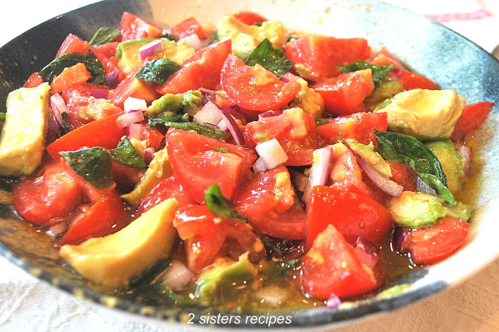 A bowl filled with sliced tomatoes, avocado, red onion, and fresh basil. 