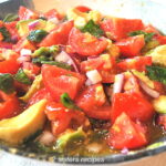 A bowl filled with sliced tomatoes, avocado, red onion, and fresh basil.