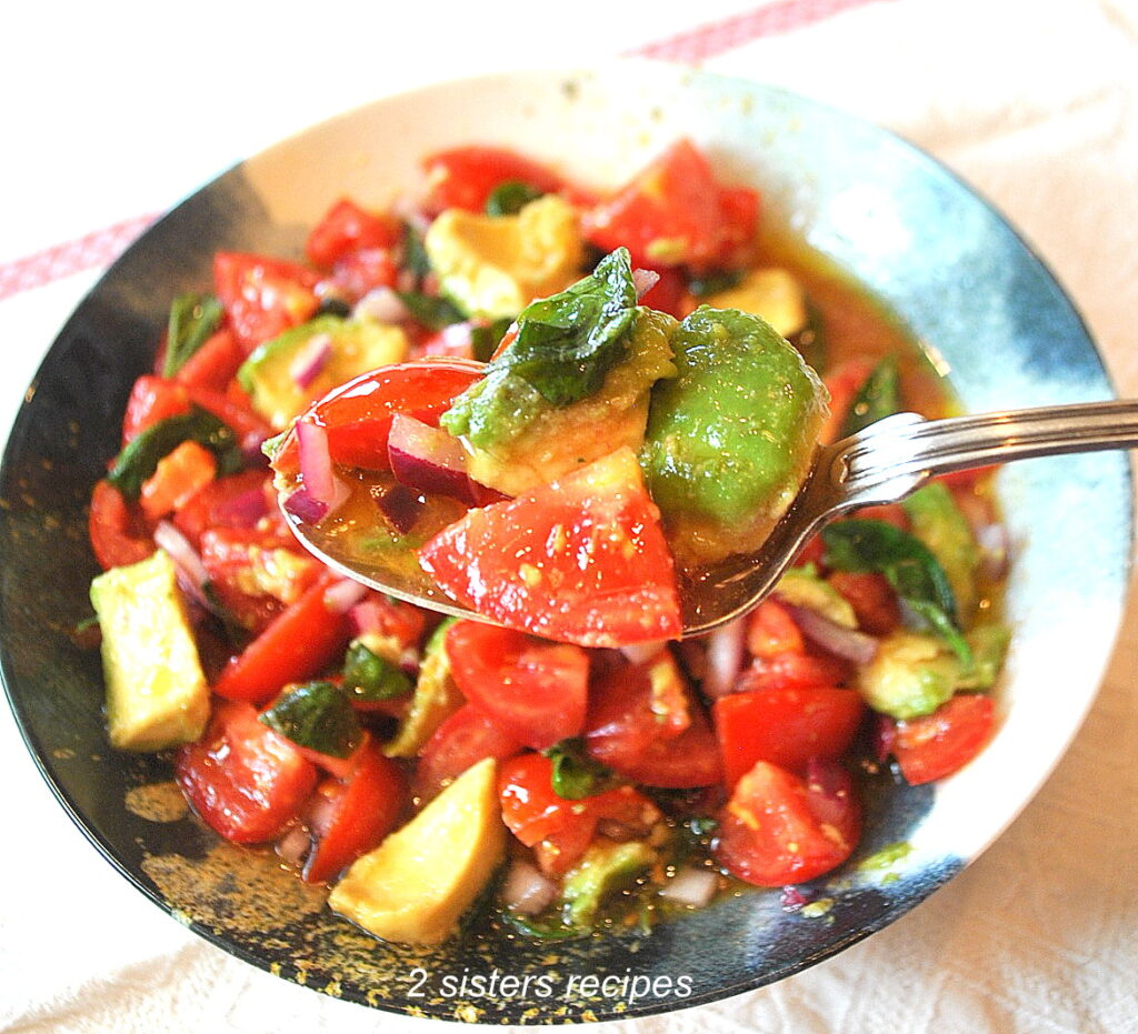 A blue and white bowl filled with a chilled tomato salad, with a spoonful of tomato, avocado and basil. 