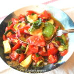 A blue and white bowl filled with a chilled tomato salad, with a spoonful of tomato, avocado and basil.