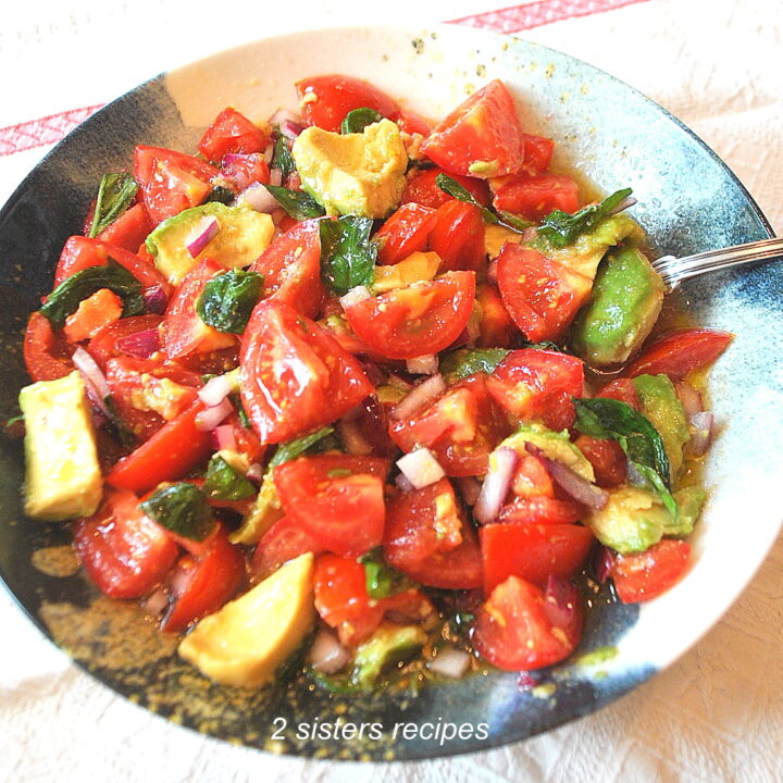 A bowl filled with quartered tomatoes, avocado and fresh basil with a spoon inside the bowl.