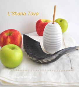 A shofar ( the black horn) and red and green apples and a jar of honey beside it.