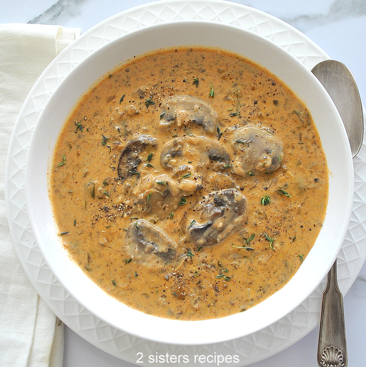 A white bowl of creamy mushroom soup with a few mushrooms on top.